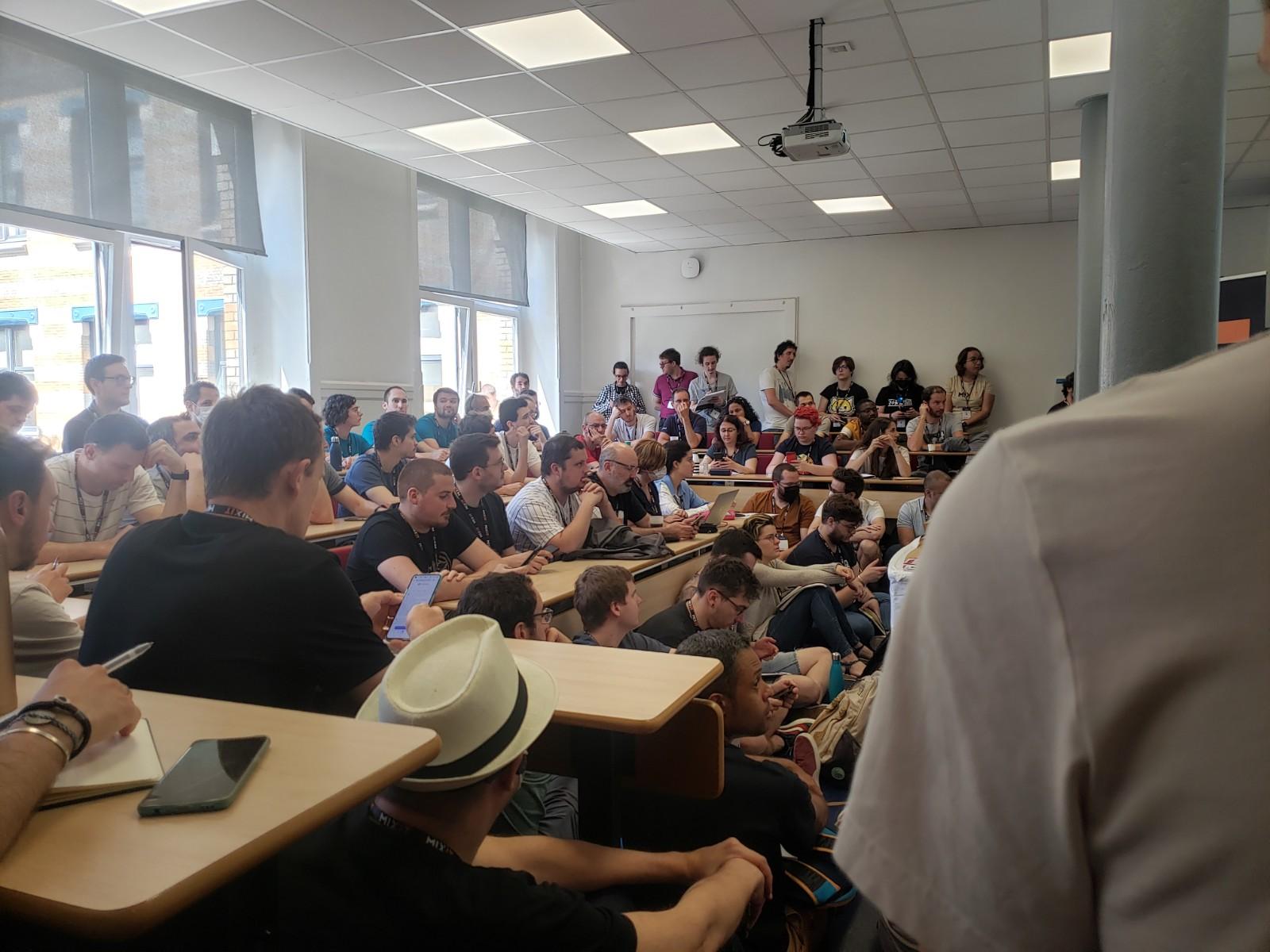 Photo du public dans une salle de cours avec des personnes assises par terre